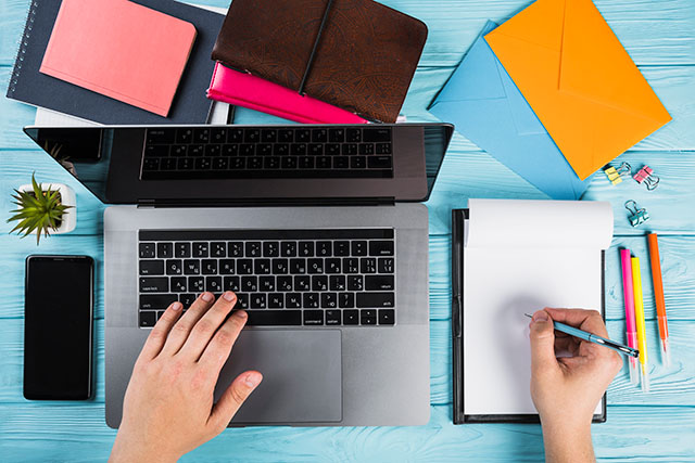 Laptop on blue table with colorful office supplies